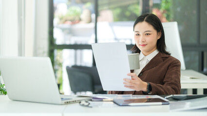 Thoughtful female entrepreneur sitting in bright modern office and checking financial reports.
