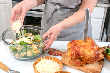 Cooking Caesar salad. Cook adds grated parmesan to glass bowl with salad in a home kitchen.