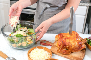 Cooking Caesar salad. Cook adds grated parmesan to glass bowl with salad in a home kitchen.