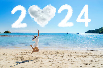 Fototapeta na wymiar Side view of a woman jumping on the beach with clouds shaped heart and 2024 new year numbers