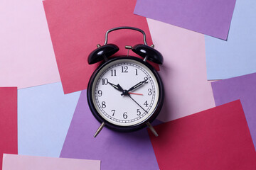Black bell alarm clock on abstract multicolored papers background. Minimal, flat lay.