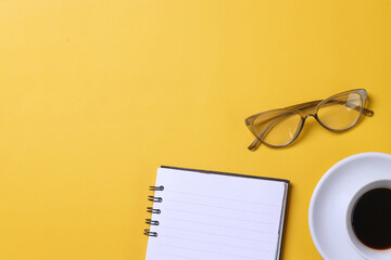 Simple office desk with notebook, cup of coffee and glasses isolated on yellow background. Minimalistic concept