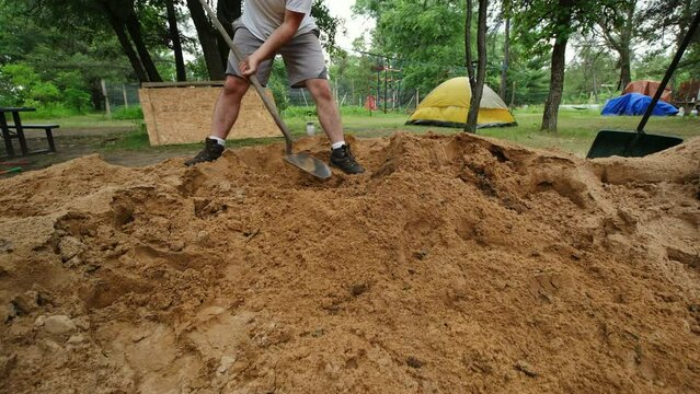 Close up of pile of sand or dirt being shoveled by man in shorts wearing boots.