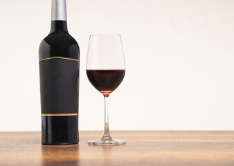 Wine bottle and a glass of red wine are on the table against a gray background.