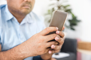 Asian man in blue shirt sitting on sofa in living room using smartphone. Holiday relaxation. Online shopping. Modern communication technology. about technology, rest, shop, relax.