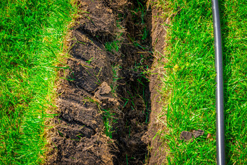 A ditch dug in the lawn for laying pipes and installing irrigation. Soil under green lawn and grass...