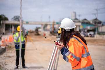 Surveyor engineers wearing safety uniform ,helmet and radio communication with equipment theodolite to measurement positioning on the construction site of the road with construct machinery background.