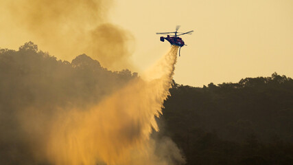 Fire fighting helicopter dropping water onto forest fire