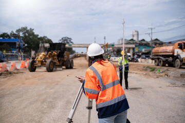 Surveyor engineers wearing safety uniform ,helmet and radio communication with equipment theodolite to measurement positioning on the construction site of the road with construct machinery background.