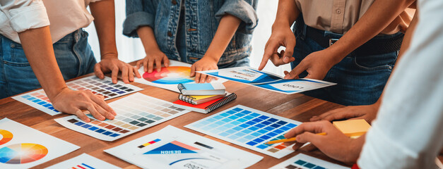 Graphic designer brainstorm logo and graphic art at busy creative studio workshop. Experiment and brainstorm color palette and pattern at workspace table for creative design. Panorama shot. Scrutinize