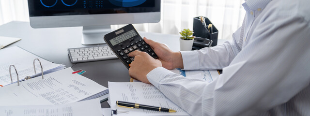 Corporate auditor calculating budget with calculator on his office desk. Dedicated accountant...