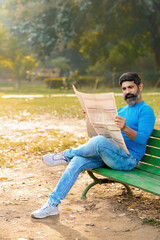 Young indian man reading news paper at park.