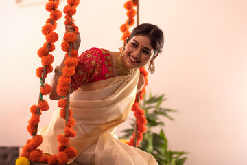 Woman in traditional clothing sitting on a swing decorated with flowers on Onam