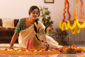 Woman in white saree decorating floor with flower garland to celebrate Onam