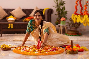 Woman in white saree decorating floor with flower garland to celebrate Onam