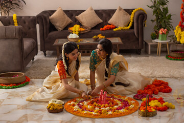 South Indian women in white saree decorating floor with flowers to celebrate Onam
