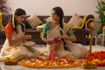 South Indian women in white saree decorating floor with flowers to celebrate Onam