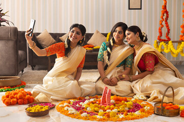 South Indian Women taking selfie while sitting near floral decoration on the occasion of Onam