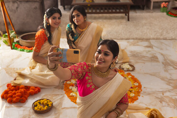 South Indian Women taking selfie while sitting near floral decoration on the occasion of Onam