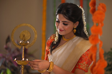 Woman in white saree lightening diya on the occasion of Onam