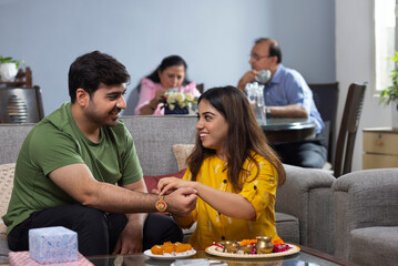 Sister tying Rakhi on her brother's wrist on Raksha Bandhan while parent sitting beside