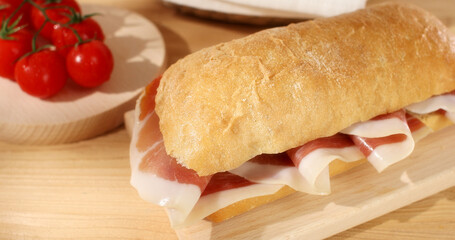 Ciabatta with Prosciutto on a wooden background. Bread basket, tomatoes and bacon or jamon sandwich. Italian food. Rustic still life. Sunny day. Close up shot.