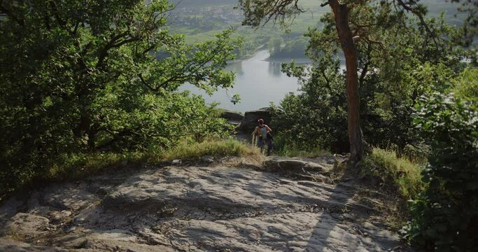 back shot young man walks hiking a mountain trail bare chest, snapback hat, mountaineer gear, climbing outdoors, looking around for a wall to climb, sunny summer weather in Durnstein, Austria, Europe.