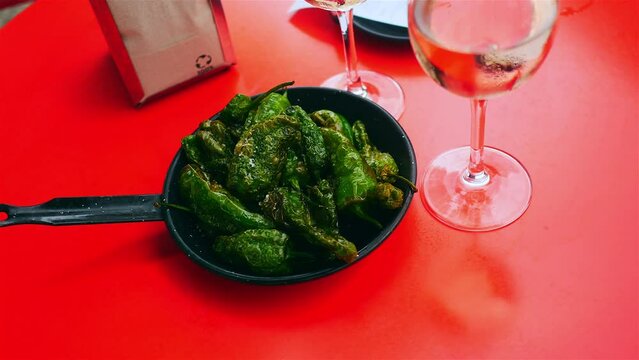 Eating padron pepper tapas with glasses of rose wine on red table