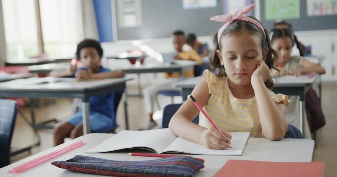 Focused diverse schoolchildren at desks learning and writing in classroom at elementary school