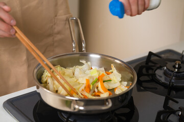 フライパンで野菜炒めを作る若い男性