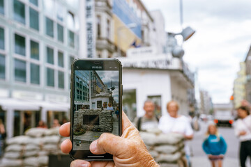 Naklejka premium Person taking a photo with an iphone at Check Point Charlie in Berlin, Germany