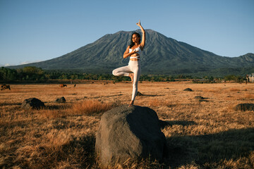 A young girl of European appearance, in a white yoga jumpsuit, meditates and practices yoga at dawn...