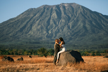 A guy and a girl, of European appearance, have fun, enjoy life, hug each other in nature, against the backdrop of the Agung volcano, in Bali.