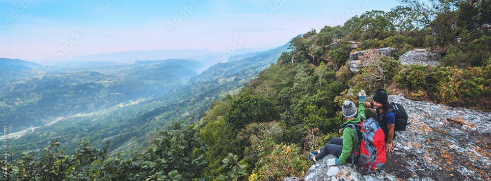 Wall mural asian lover women and men travel nature. travel relax. watch mountain view. on a cliff on the mounta