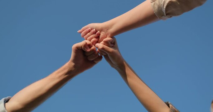 Three friends are banging their fists against the blue sky. Gesture of celebration and joy in teamwork