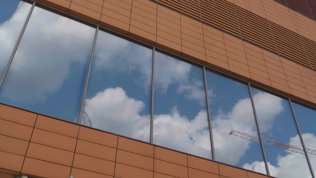 Blue sky with white clouds reflecting in tinted windows of building, camera panning left