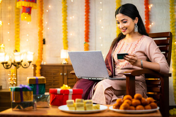 Happy young indian girl making online shopping on laptop using credit card during festival sales at...