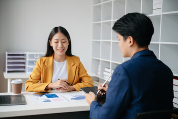 Asian business colleague business presents and explains and using laptop and tablet. Teamwork, financial marketing team,   while sitting in modern office room..
