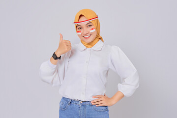 Smiling happy young Asian Muslim woman wearing a hijab showing thumb up sign isolated over white...