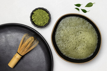 Bamboo whisk on a black plate. Matcha tea in a black bowl. Green matcha tea powder in a bowl.