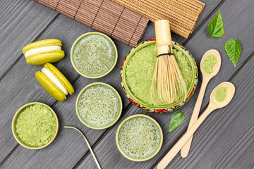 Bamboo whisk in bowl with matcha powder. Matcha green tea, macaroni cakes and wooden spoons on table