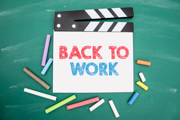 Back To Work. Film clapper and colored pieces of chalk on a green chalkboard background