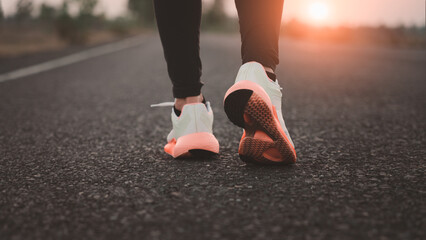 Adult woman doing exercise walking and running on the country road in the morning with sunrise background, concept of health and lifestyle.