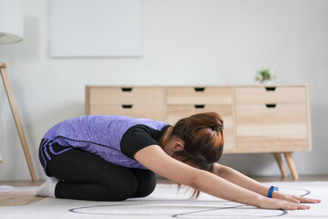 Young asian woman doing yoga exercise with child pose on the floor for healthy lifestyle at home