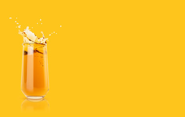 Apple yellow cold transparent juice in glass with reflection, bright splashes, drops flying, swirl colorful yellow background, copy space. Refreshing healthy summer gold pear beverage with splashing.