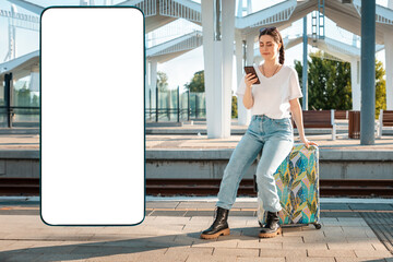 Young woman sitting on her luggage and waiting departure from train station using cellphone. Big...