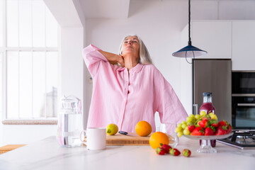 Woman stretching neck standing in kitchen at home