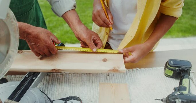 An elderly man in an apron teaches his grandson to use a miter saw, close-up of hands, no face
