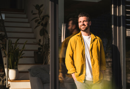 Happy Man With Hands In Pockets Leaning On Glass