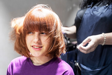 teenage girl with a fashionable bob haircut in a hairdressing salon on styling her hair. Fashion &...